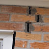 A brick wall displaying stair-step cracks and messy tuckpointing on a Spring Valley home
